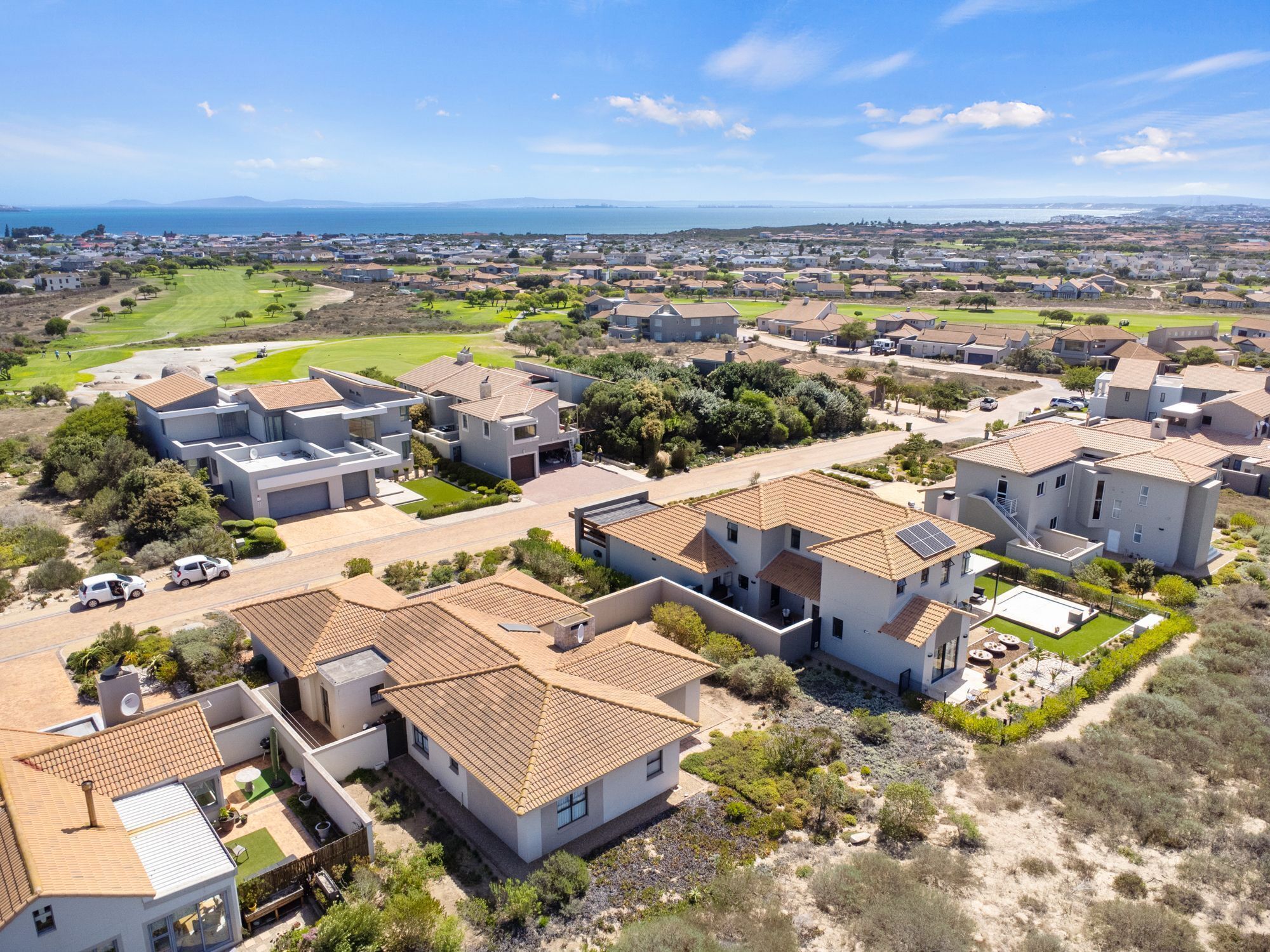 Un quartier résidentiel avec des maisons modernes, un terrain de golf et une vue sur la côte.