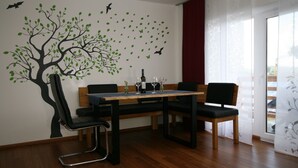 Un comedor con una mesa de madera, sillas negras y un adhesivo mural de un árbol con pájaros.
