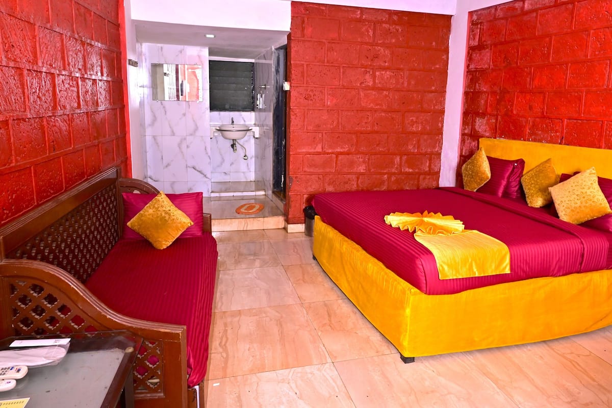 A hotel room with a red brick wall, a bed with a yellow and red bedspread, and a wooden headboard.
