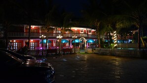 A multi-story building with a red and white facade, multiple balconies, and a central entrance with a covered walkway. - We Hotels Alibaug (Alibag)
