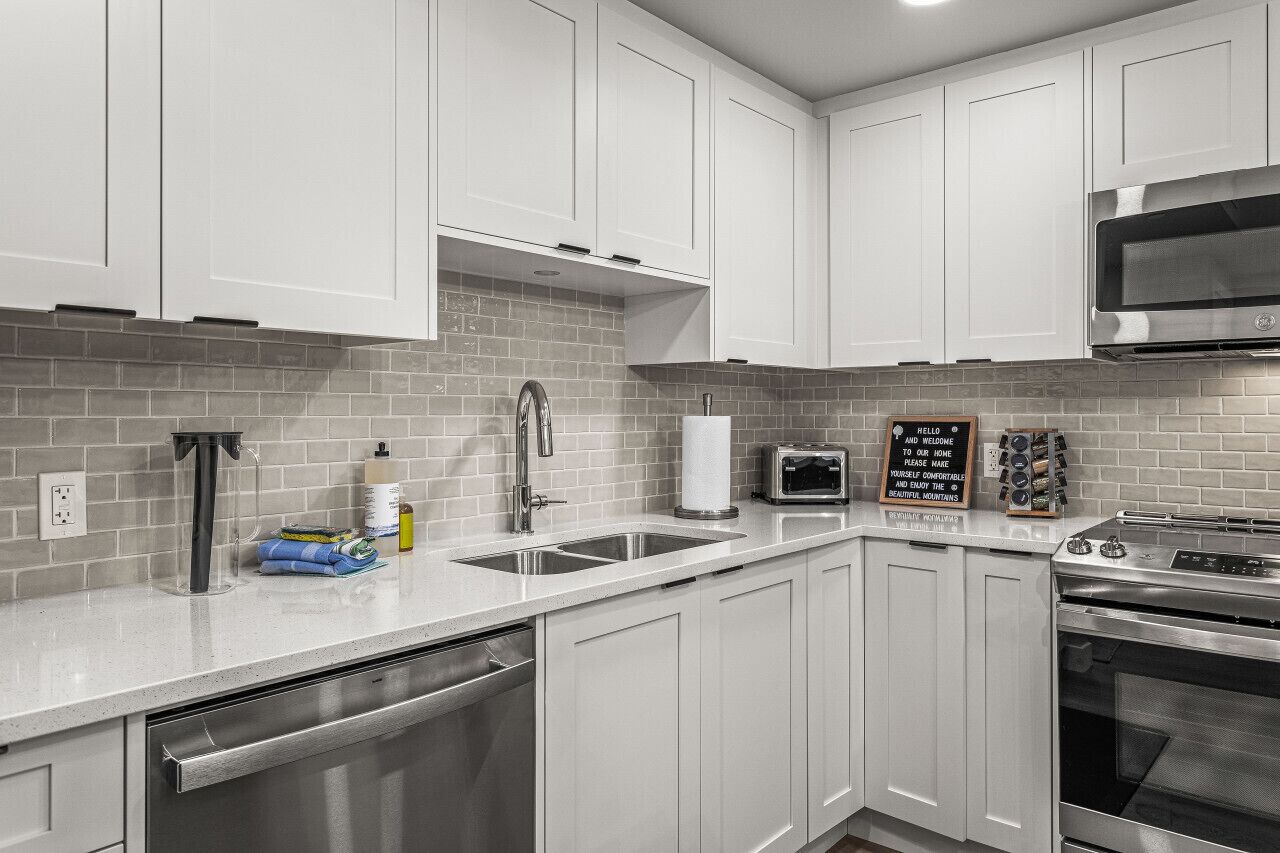 A modern kitchen with white cabinets, a stainless steel sink, a microwave, and a stove.