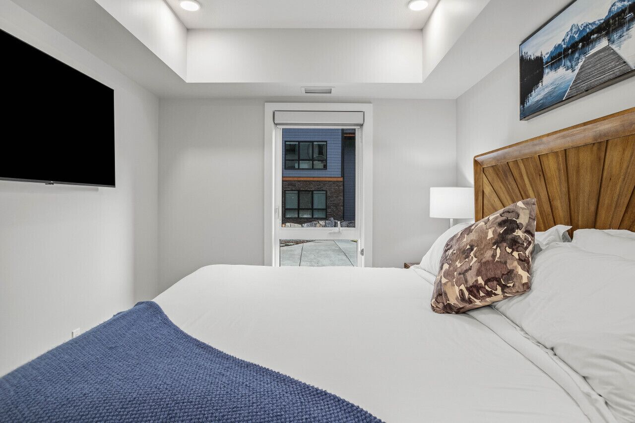 Ein modernes Hotelzimmer mit einem großen Bett, einem Fernseher und Blick auf ein Gebäude durch eine Glasdoor.