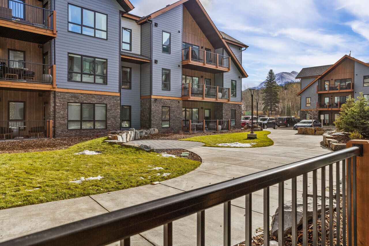 A multi-story residential building with balconies, a landscaped courtyard, and a mountain view in the background.