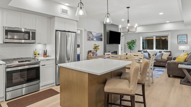 Una cocina moderna con armarios blancos, electrodomésticos de acero inoxidable y una isla central con taburetes de bar.