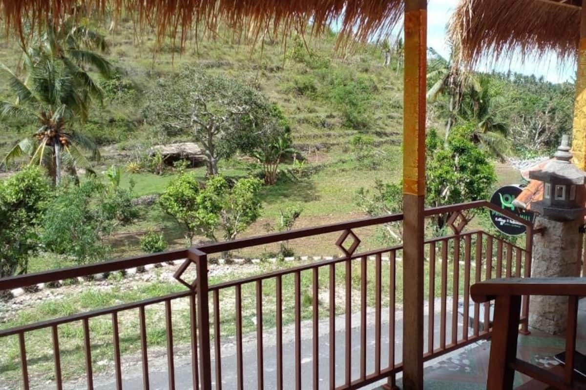Varanda com vista para uma paisagem exuberante, incluindo árvores e uma construção com telhado de palha.