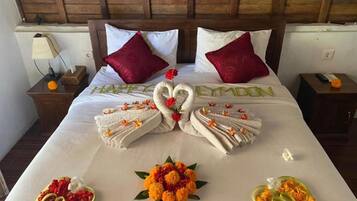 Habitación de hotel con una cama bien hecha, dos almohadas rojas, una mesita de noche con lámpara y un cuadro en la pared.