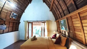 Een slaapkamer met een houten gewelfdak, een bed met een beige dekbedovertrek en een nachtkastje met een lamp.