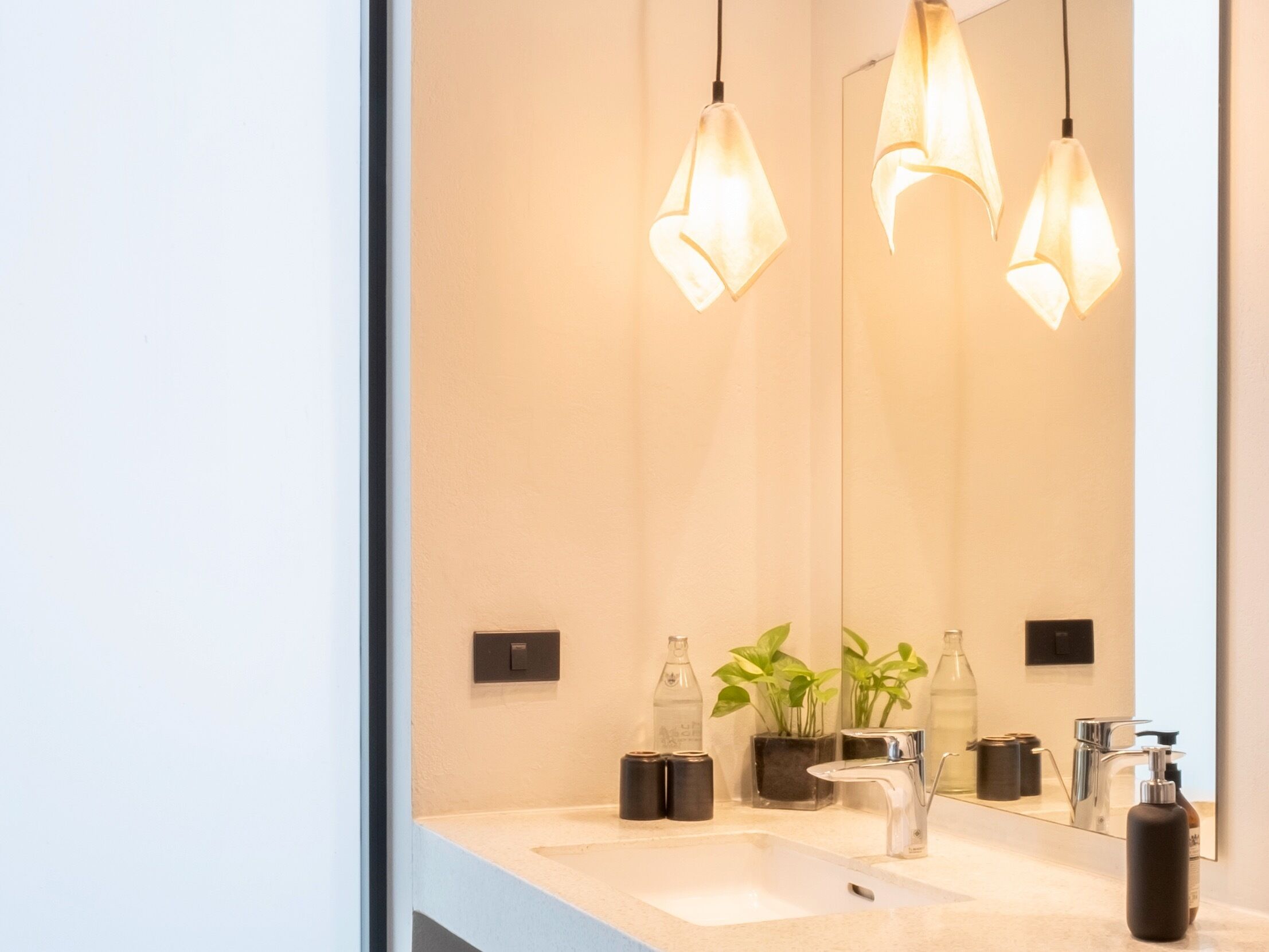 A modern bathroom with a large mirror, two sinks, and pendant lights.