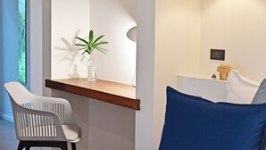 Une chambre moderne avec une chaise blanche, une petite table sur laquelle est posée une plante, un coussin bleu et une étagère en bois.