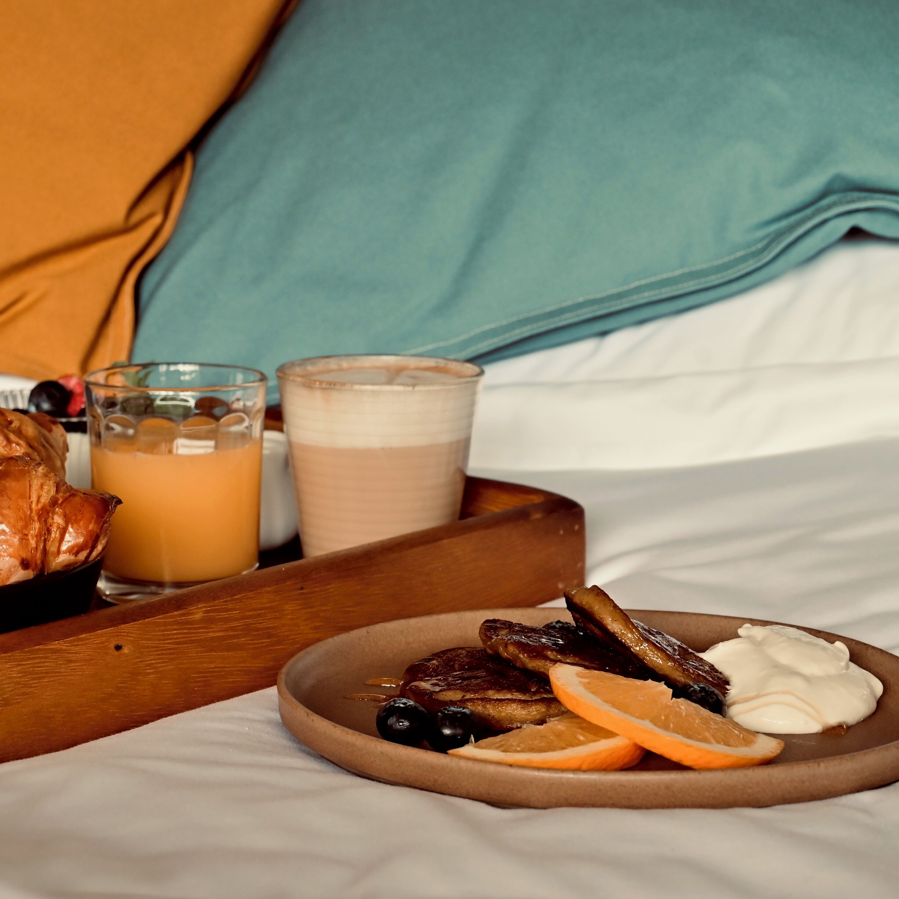A breakfast tray with toast, fruit, and a glass of orange juice on a bed.