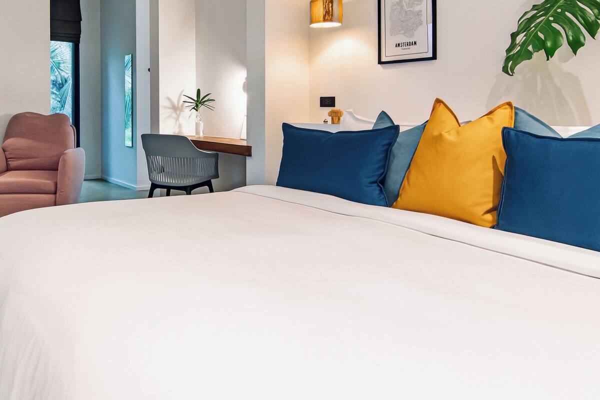 A modern hotel room with a large bed, a desk, a chair, and a large window with a view.