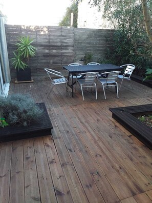Un patio al aire libre con terraza de madera, una mesa redonda con sillas y plantas en macetas.