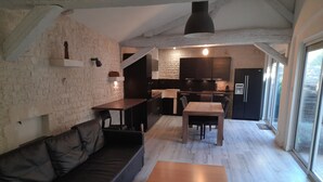 Un espacio habitable moderno con piso de madera, un sofá negro, una mesa de madera y una zona de cocina con armarios oscuros.