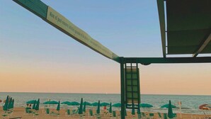 Blick auf einen Strand mit einem Schild, auf dem 'Hotel Astoria' steht und eine Nachricht auf Italienisch zu sehen ist.