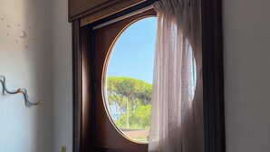 Ein Zimmer mit einem Einzelbett, einem runden Fenster mit Vorhang und einem an der Wand befestigten Haken.