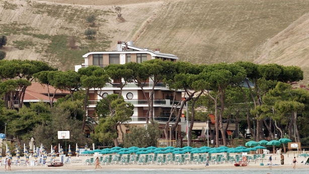 A hotel with a pool area, beach chairs, umbrellas, and a mountainous backdrop. - Hotel Astoria (Pineto)