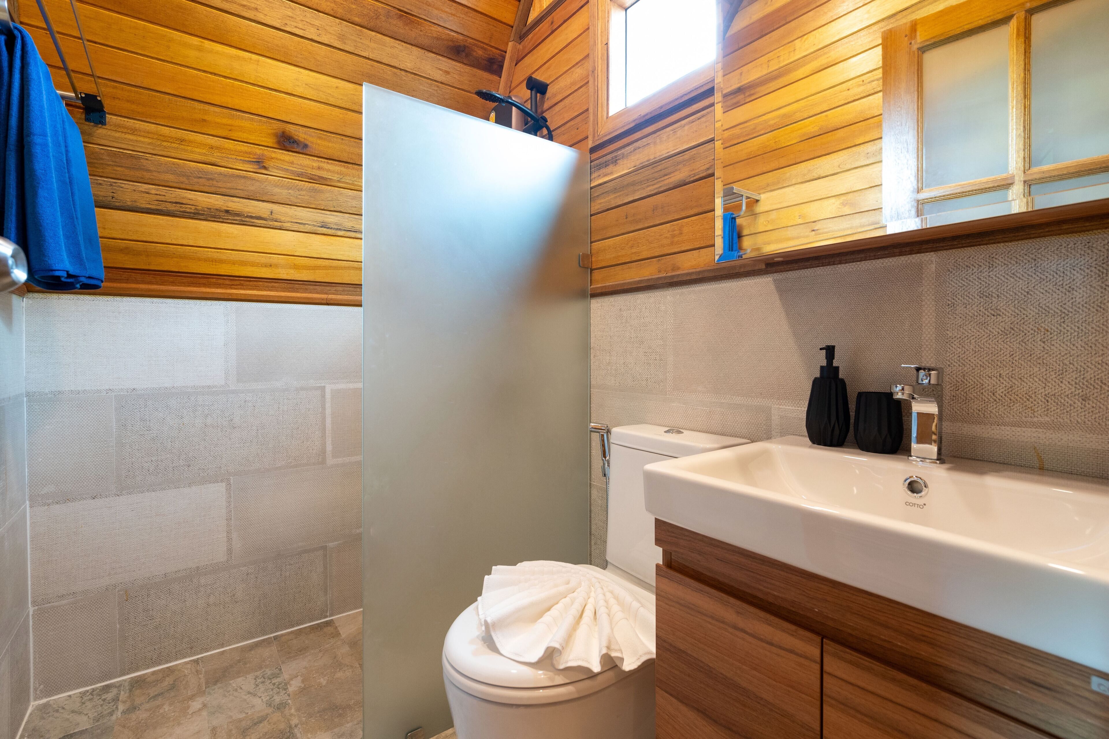 A bathroom with a wooden ceiling, a white toilet, a sink with a mirror, and a towel on the toilet seat.