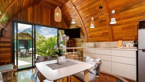 A cozy wooden interior with a dining area, kitchen, and large sliding glass doors leading to an outdoor patio. - Chalet Style 2BR Pool Villa Pasak 1 (Choeng Thale)