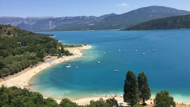 Eine Küstenlandschaft mit Strand, Booten und Bergen im Hintergrund.