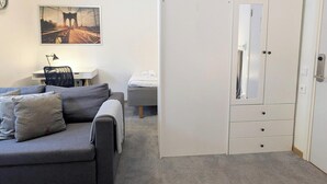 Une chambre avec un canapé gris, un bureau avec une lampe, un lit, une armoire et un tableau représentant un pont.