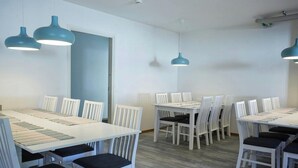 Une salle de conférence avec des tables et des chaises blanches, des suspensions bleues et une porte blanche.