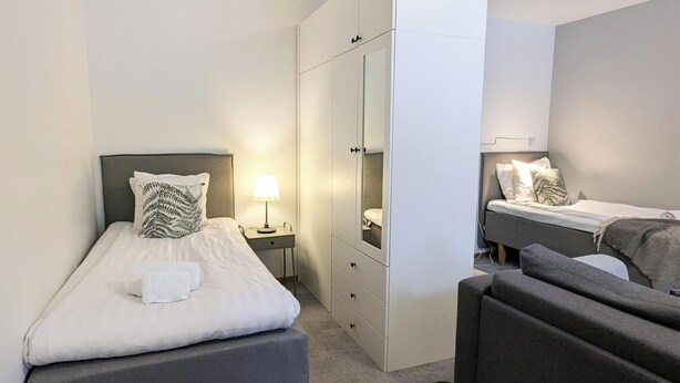 Une chambre d’hôtel de taille réduite, équipée de deux lits simples, d’une armoire, d’un bureau et d’une chaise.