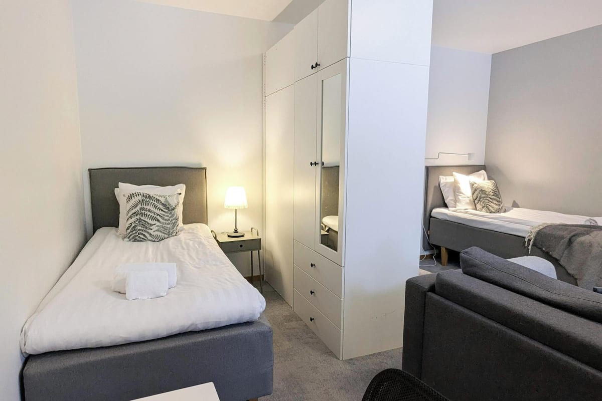 A compact hotel room with two single beds, a wardrobe, a desk, and a chair.