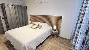 Una cama bien hecha con cabecera de madera, una mesita de noche con lámpara y una cortina en la ventana.