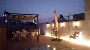 An outdoor patio area with a glass floor, white chairs, a table, and string lights. - Hostel Ibarra by Bossh! Hotels (Seville)