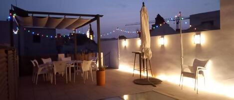 An outdoor patio area with a glass floor, white chairs, a table, and string lights.