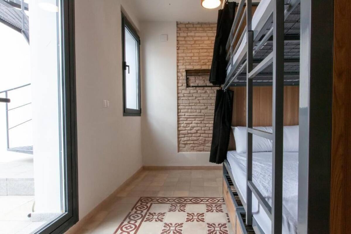 A narrow hallway with a patterned rug, a brick accent wall, and a bed with white bedding.