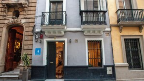 A building with a classic architectural style, featuring a central entrance with a staircase, a blue sign indicating a public area, and a door with a metal gate. - Hostel Ibarra by Bossh! Hotels (Seville)