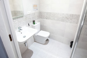 A bathroom with a white sink, toilet, and shower. There is a sign on the wall and a trash can near the toilet. - Hostel Ibarra by Bossh! Hotels (Seville)