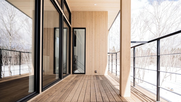 Una terraza de madera con ventanas amplias y barandilla metálica.