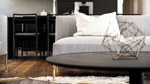 Una sala de estar moderna con un sofá gris, una mesa de centro redonda y un comedor al fondo.