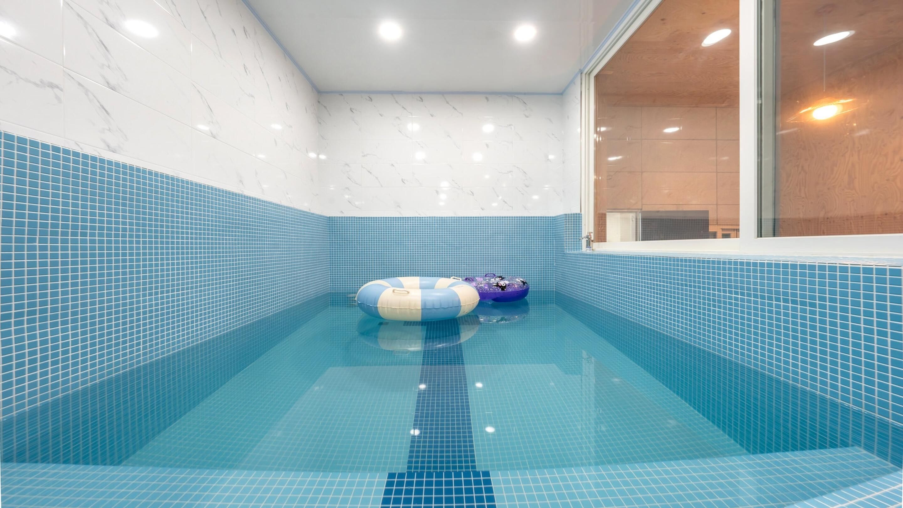 Una piscina con azulejos azules, dos flotadores inflables y un marco de ventana de madera.