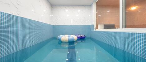 Una piscina con azulejos azules, dos flotadores inflables y un marco de ventana de madera.