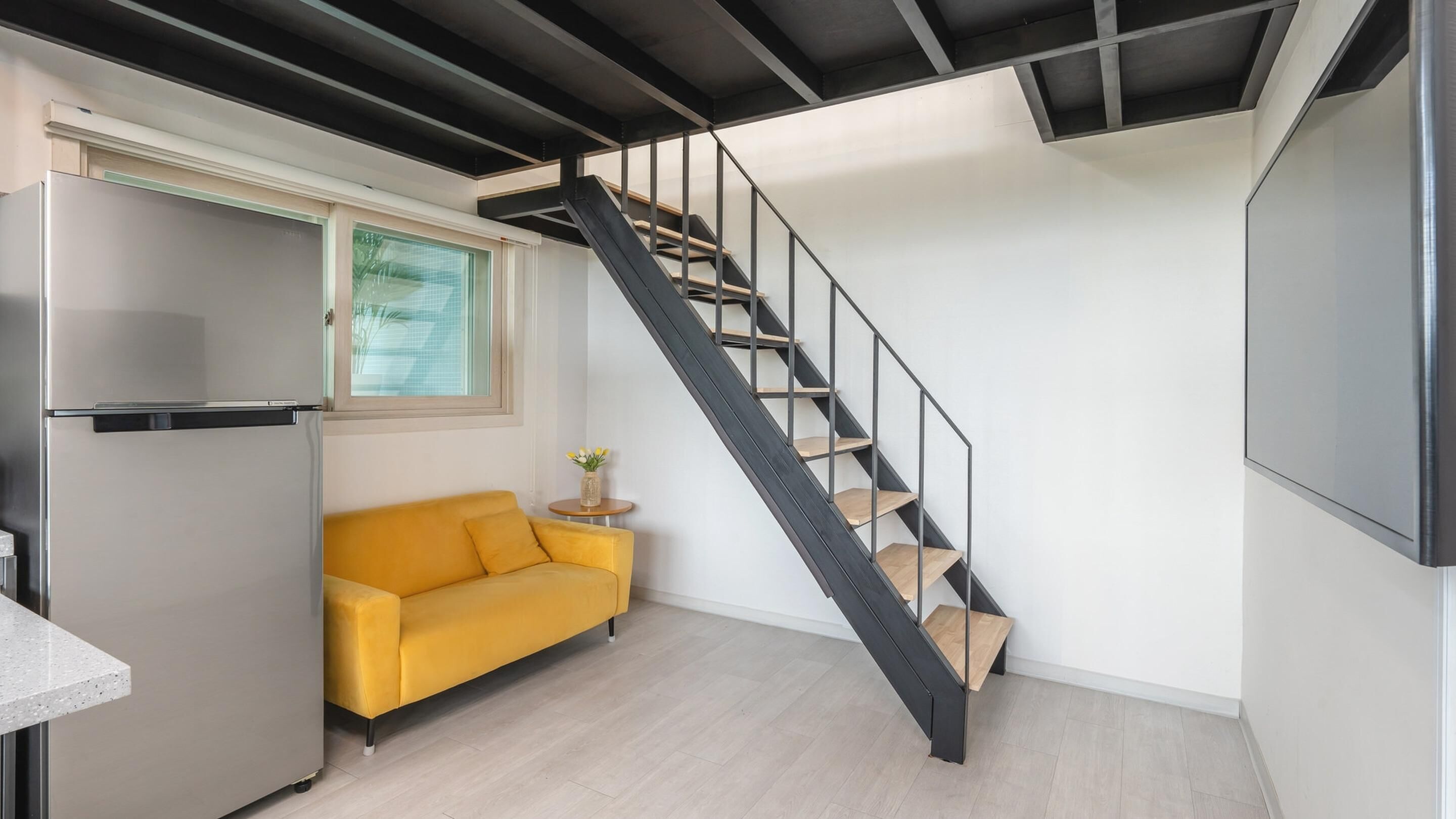 A compact living space with a kitchen, a sofa, and a staircase.