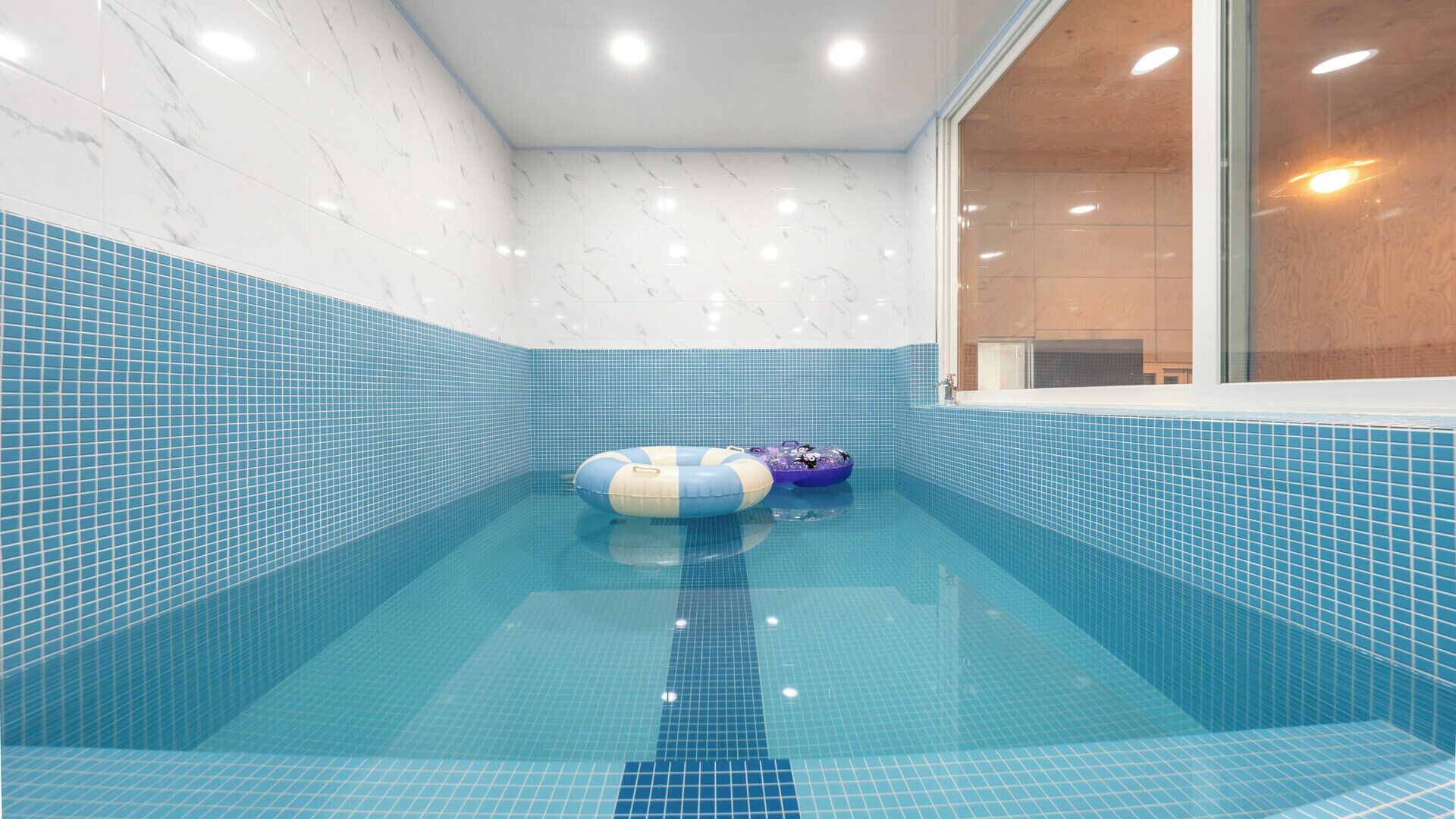 A swimming pool with blue tiles and two inflatable toys.