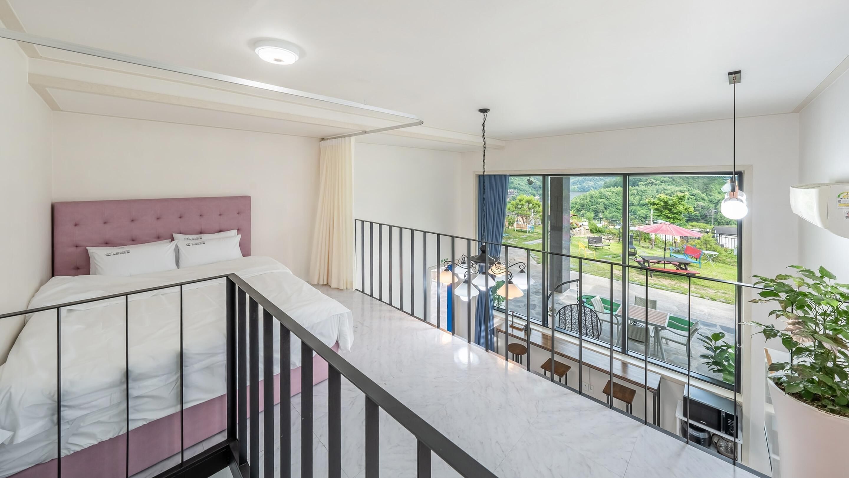 A bedroom with a bed, a balcony with a railing, and a view of the outdoors.