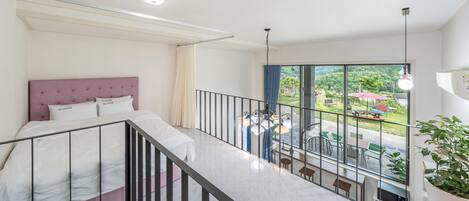 A bedroom with a bed, a balcony with a railing, and a view of the outdoors.