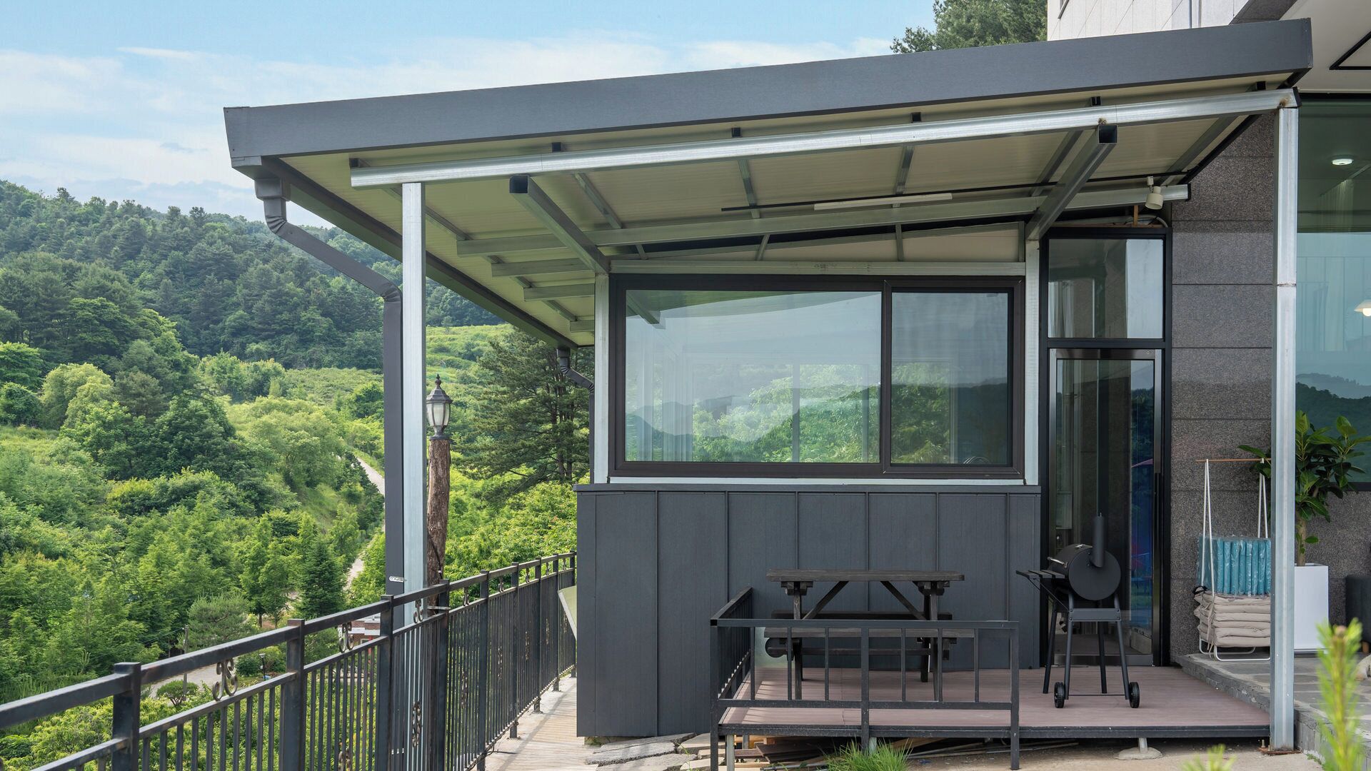 A modern building with a covered balcony, large windows, and a view of a forested hillside.