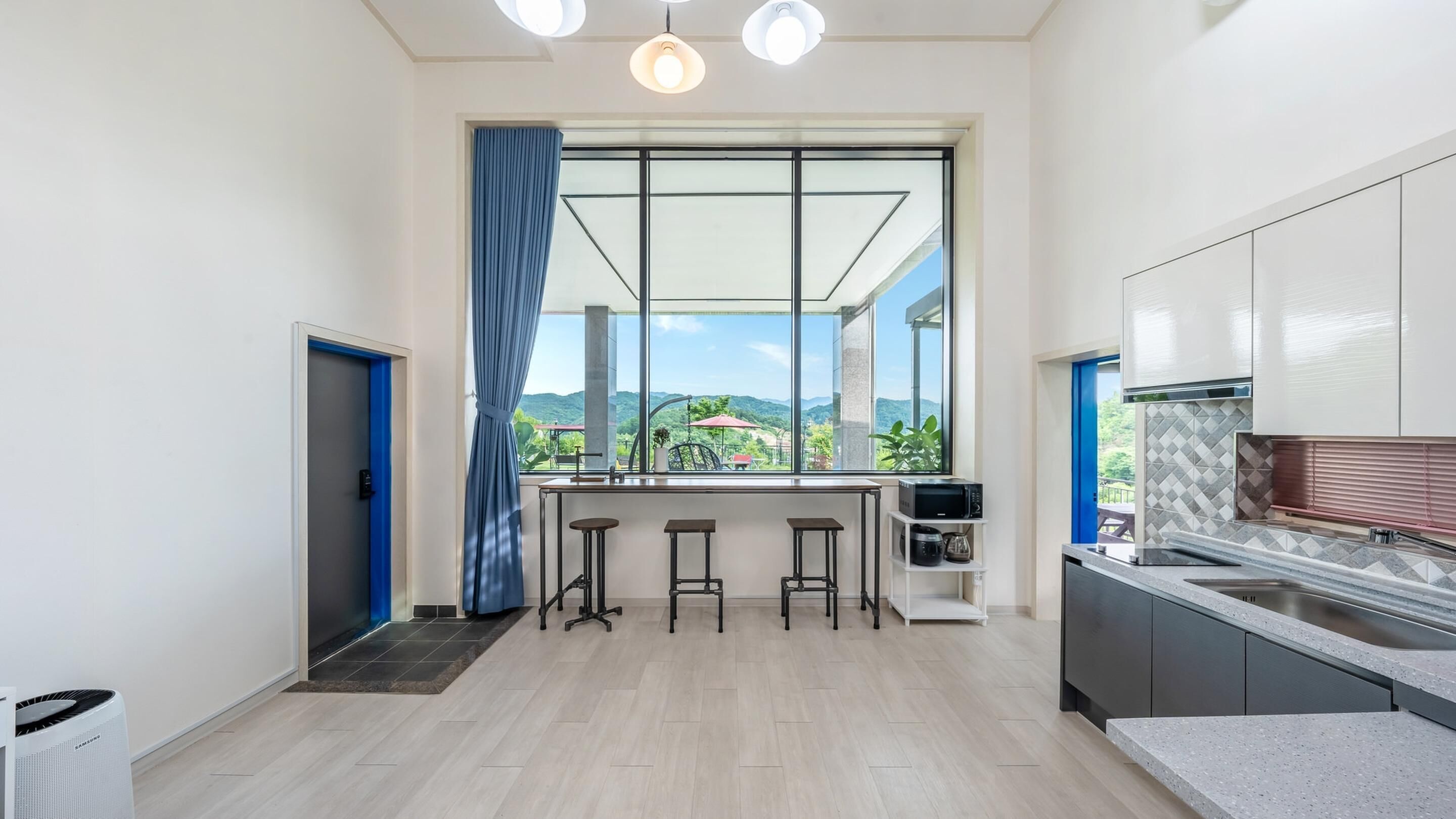 Eine moderne Küche mit großem Fenster, Barhocker und Blick ins Freie.