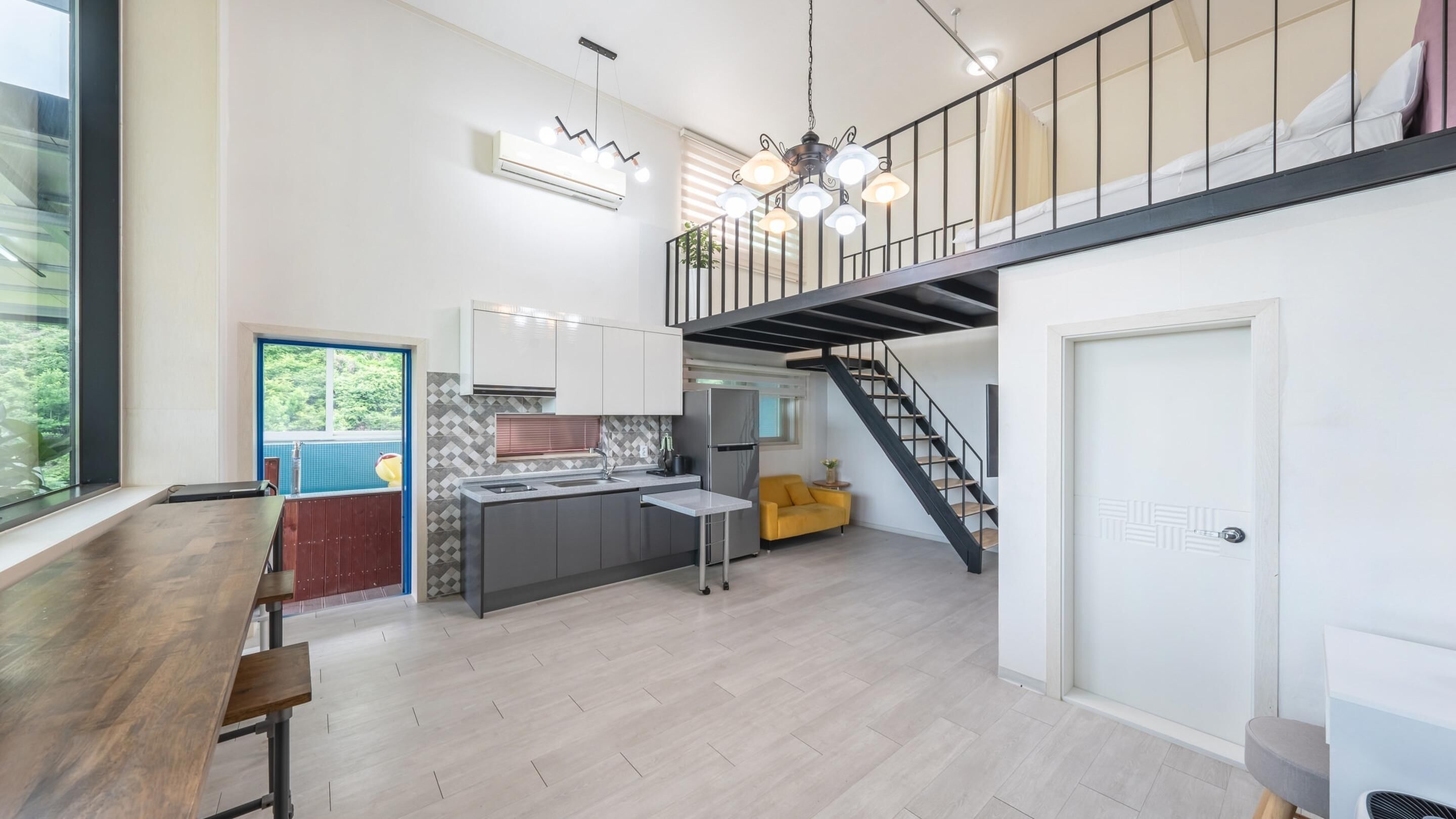 A spacious kitchen with a central island, a dining area with a wooden table, and a staircase leading to a loft bedroom.