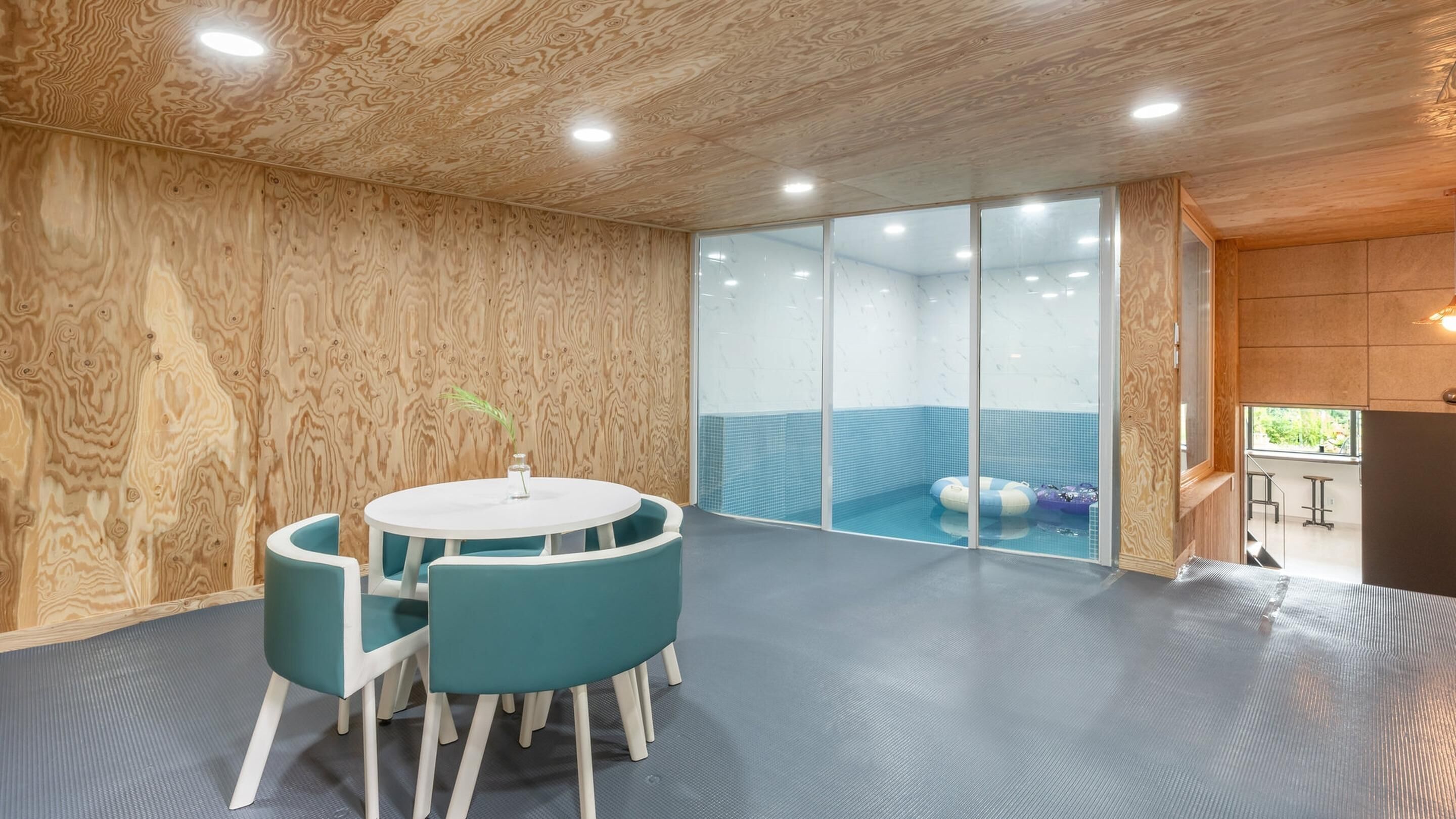 A room with a wooden ceiling, a glass partition, a pool area, and a table with chairs.