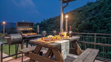 An outdoor dining area with a grill, picnic table, and wine glasses.