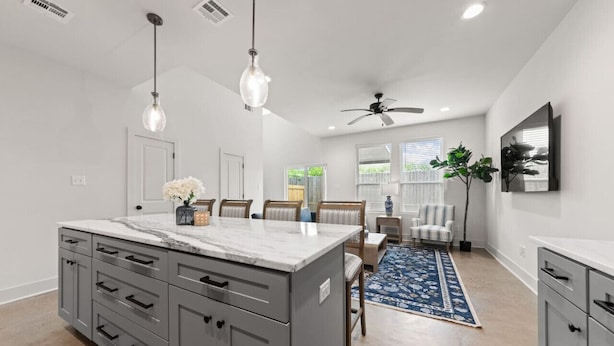 A modern kitchen with a marble island, grey cabinetry, and pendant lighting.