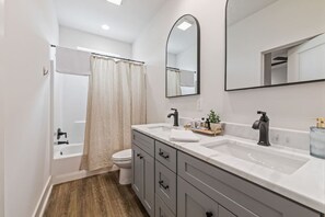 A modern bathroom with a bathtub, toilet, and vanity with a mirror. - Cajun French House*2 King Beds*Fast Wi-Fi*Garage (Lafayette)
