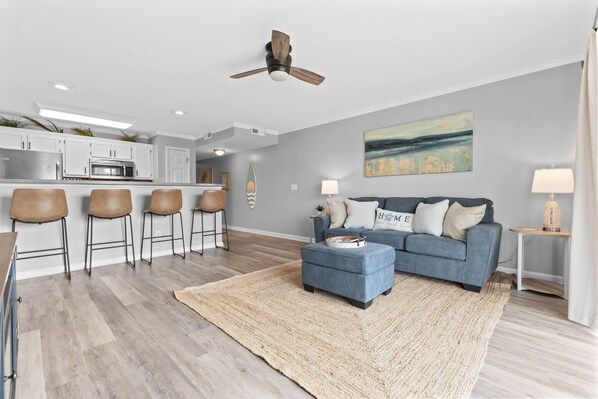 A modern living room with a blue sofa, a coffee table, and a kitchen area with bar stools.