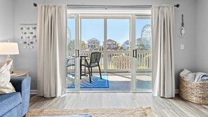 A modern living room with a blue sofa, a coffee table, and a blue rug. There is a sliding glass door leading to an outdoor patio with a table and chairs. - Carolina Yacht A2 Sum (Little River)
